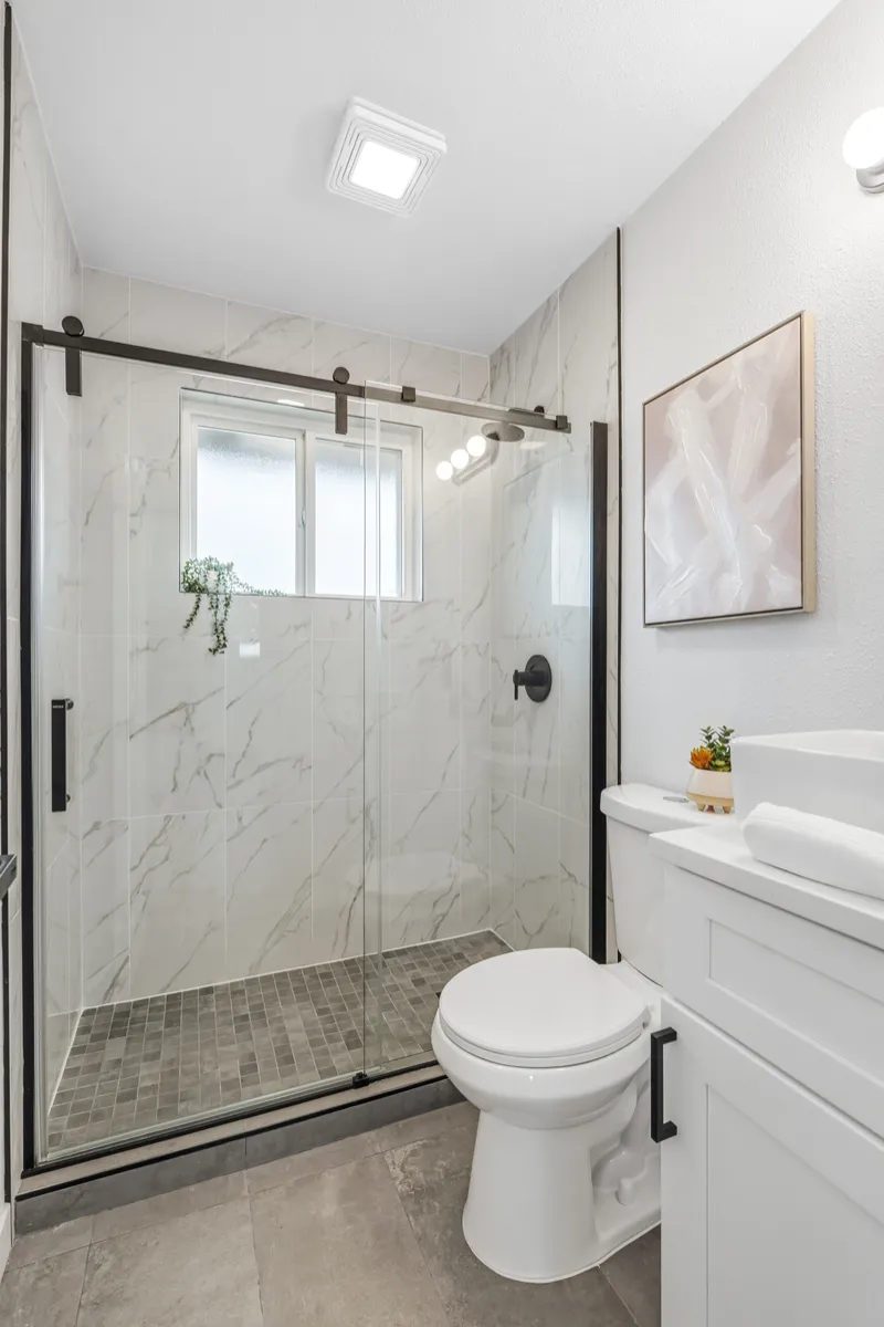 Marble-look tile shower with matte black fixtures and frameless sliding glass door