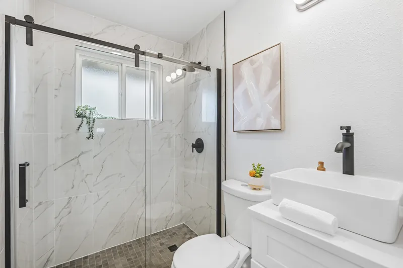 Walk-in shower with marble-look tile, black sliding glass door and vessel sink vanity