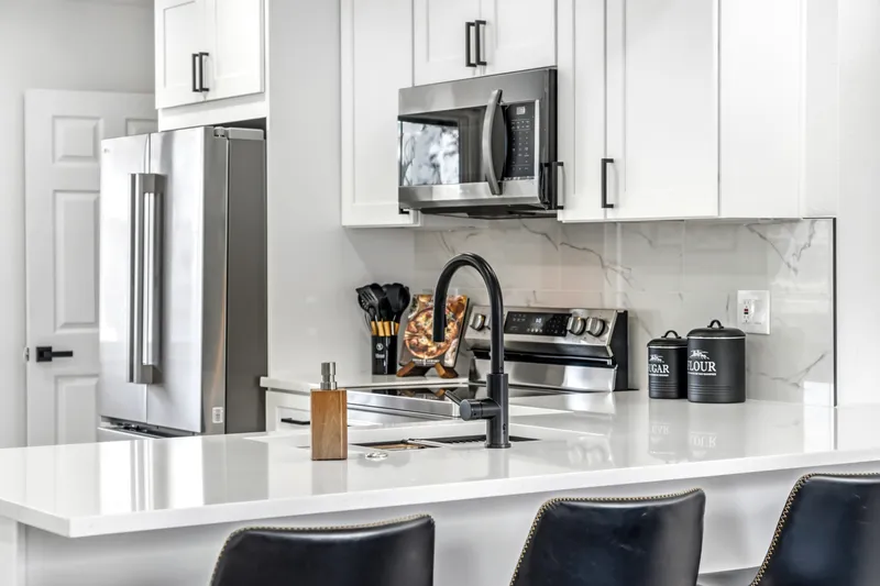 Quartz peninsula with matte black faucet and white shaker cabinets with black pulls