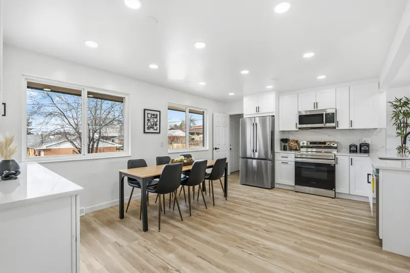 Bright white shaker kitchen with stainless range and refrigerator beside large windows