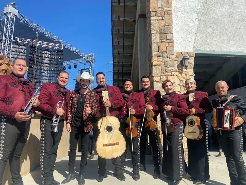 Mariachi Juvenil Grullense con trajes de charro color vino junto a un escenario de festival