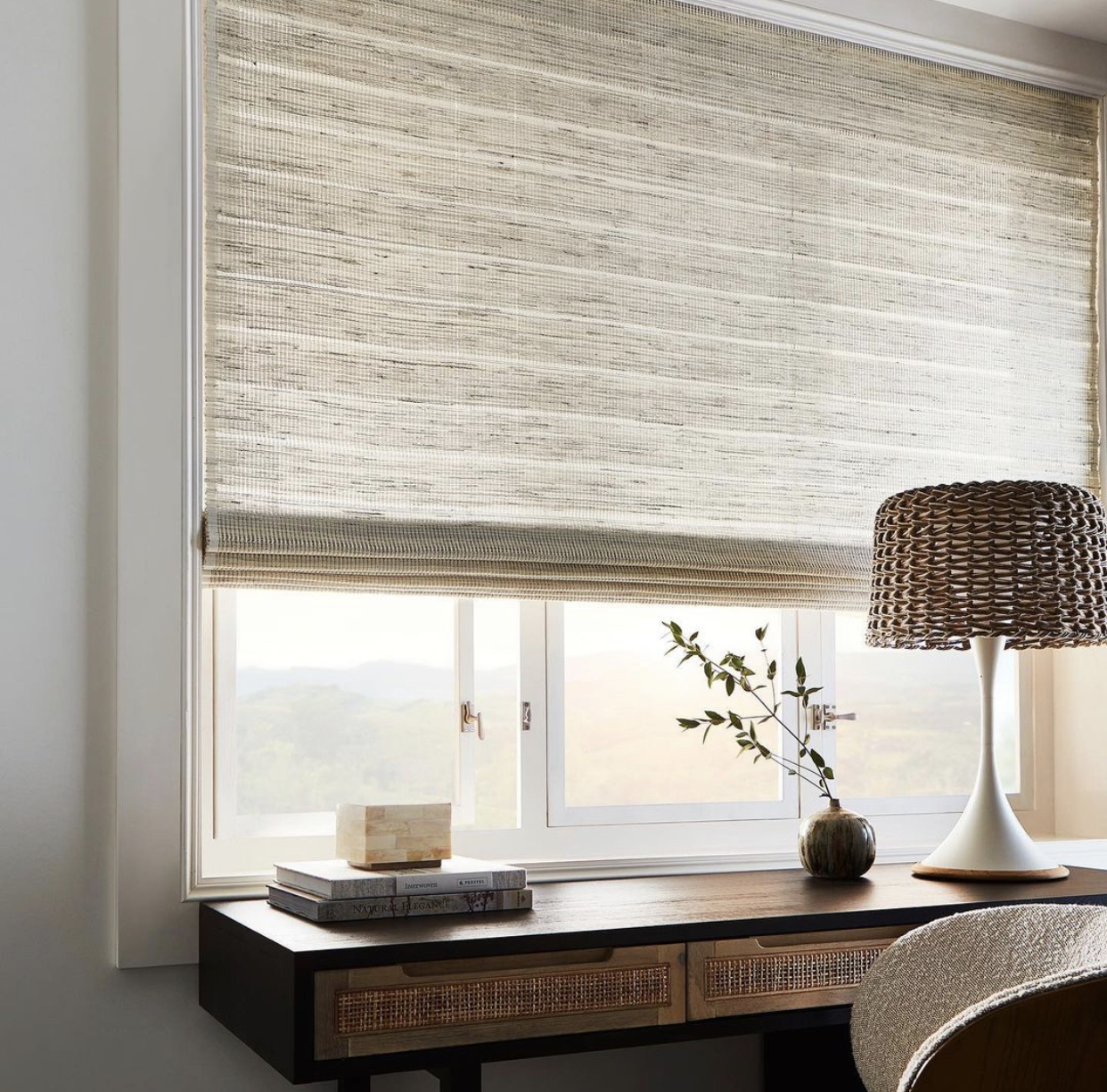 Woven natural-fiber roman shade lowered over a home office desk beside a table lamp