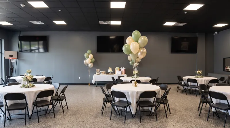 Open event room set for a birthday party with round tables, cream linens and balloons