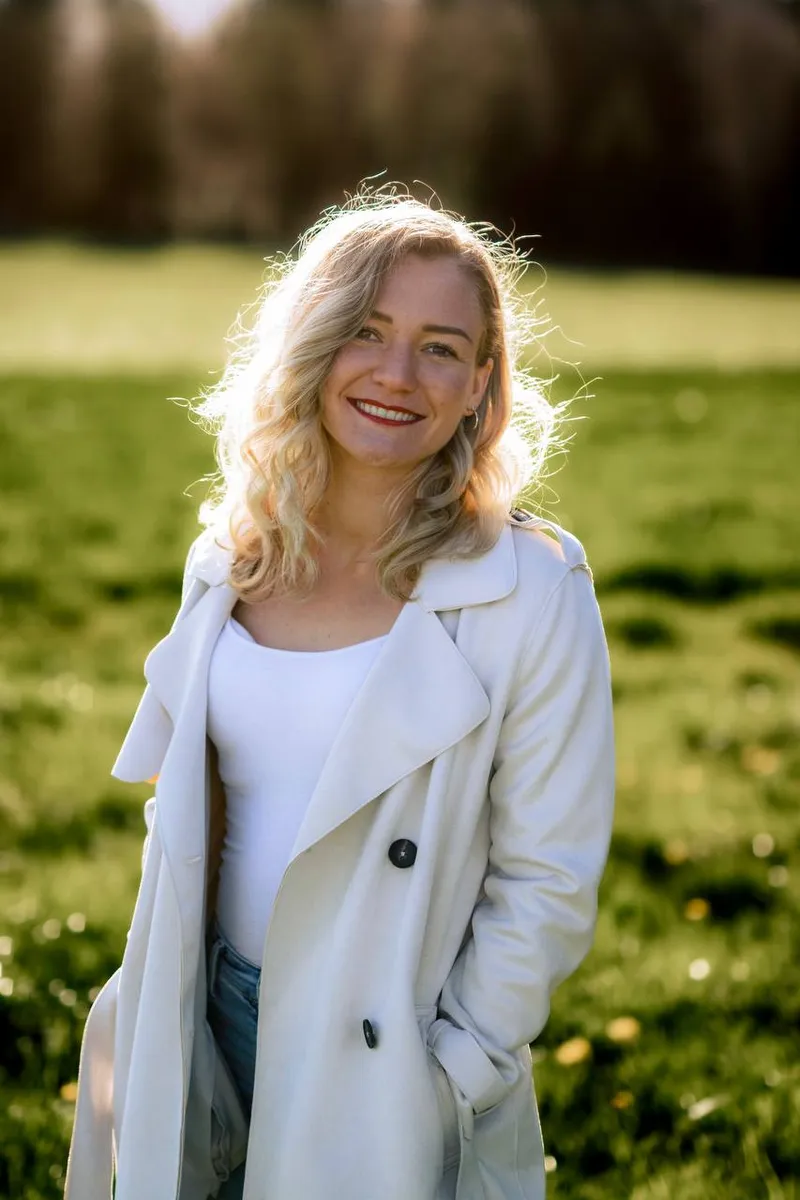 Eva Felder, Hebamme, im Trenchcoat auf einer Wiese
