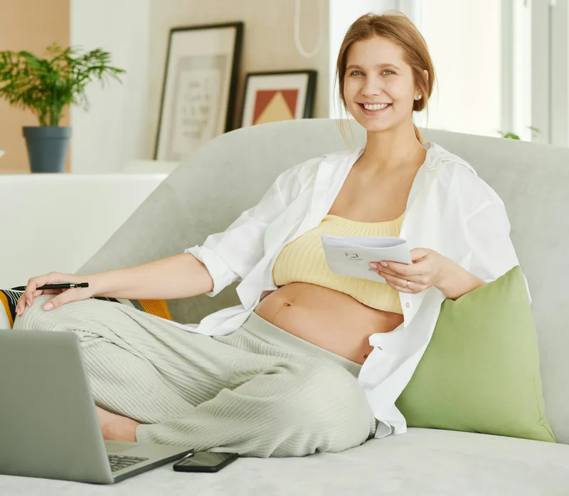 Schwangere Frau mit Laptop auf dem Sofa