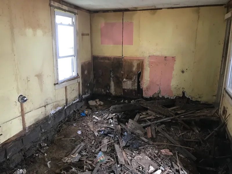Room with water-damaged walls and a debris-covered floor