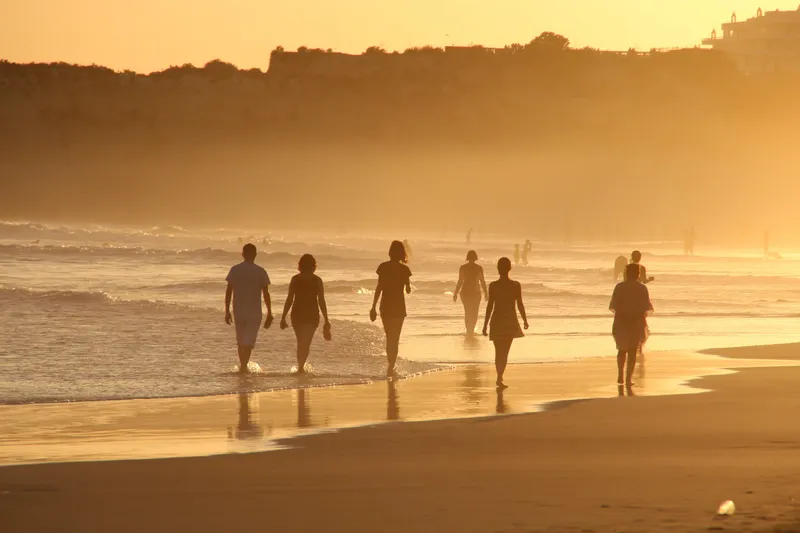 group of people walking along the beach at sunset