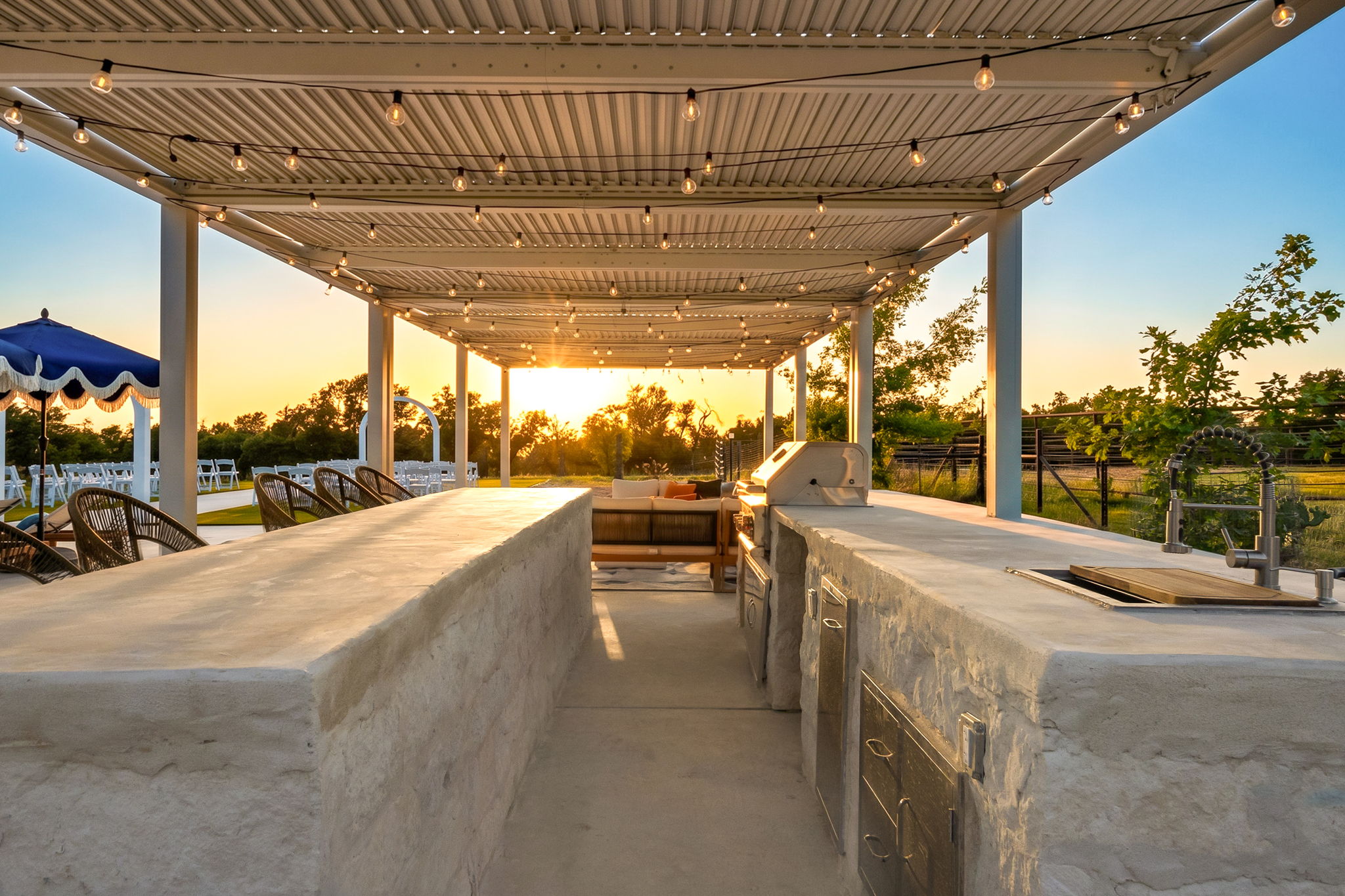 Covered outdoor kitchen with a concrete bar and grill looking out over the Hill Country at sunset