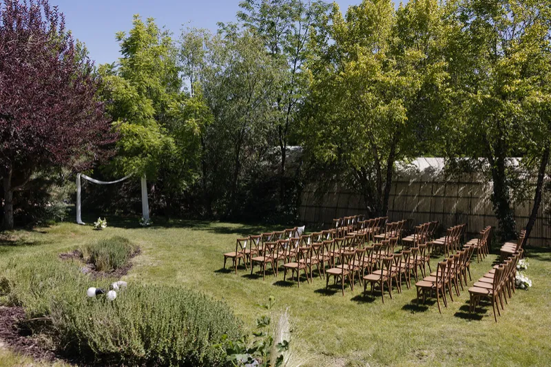 Wooden ceremony chairs arranged on the lawn beneath mature trees
