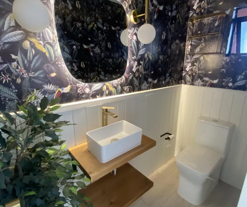 Baño remodelado con papel mural, vanitorio de madera y espejo iluminado