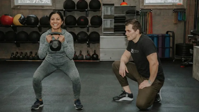 A member trains with a kettlebell alongside her coach