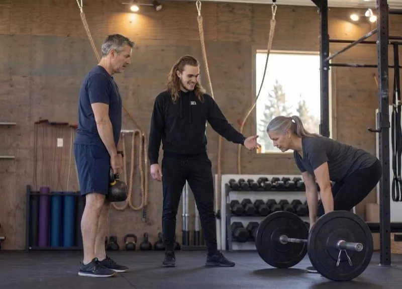 Coach Brett coaching two members through a barbell deadlift and a kettlebell deadlift