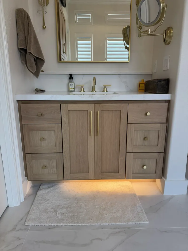 Oak bathroom vanity with brass fixtures and a lit toe kick