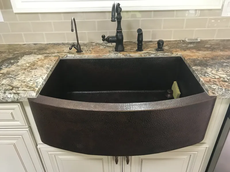 Hammered copper farmhouse sink set in cream cabinetry with granite