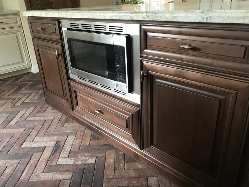 Raised-panel wood cabinets with a built-in microwave over a brick floor