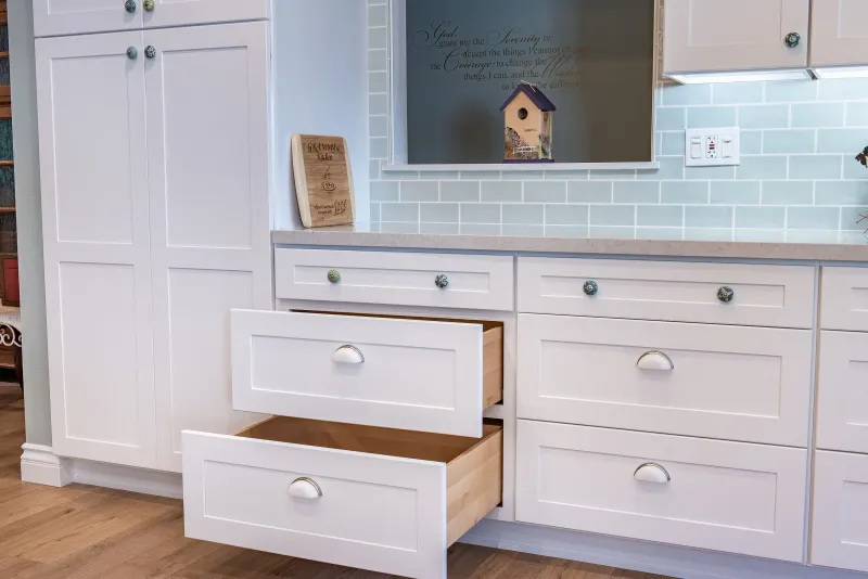 White shaker cabinets with deep drawers open below a seafoam tile backsplash
