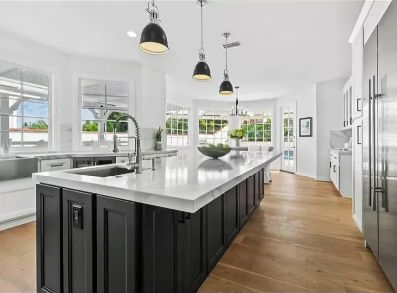 Wide view of a black island with a white perimeter and wood floors