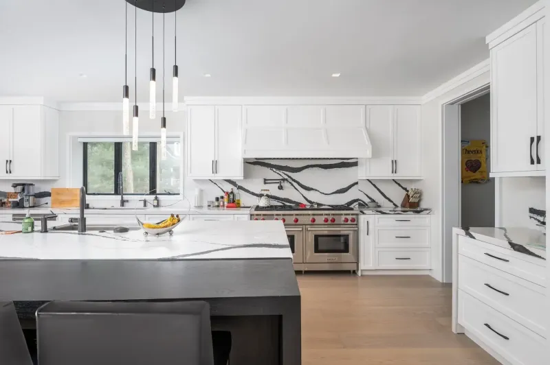 Fort Salonga: a white kitchen with a black-veined marble backsplash behind the range, a black island and a cluster of slim pendants