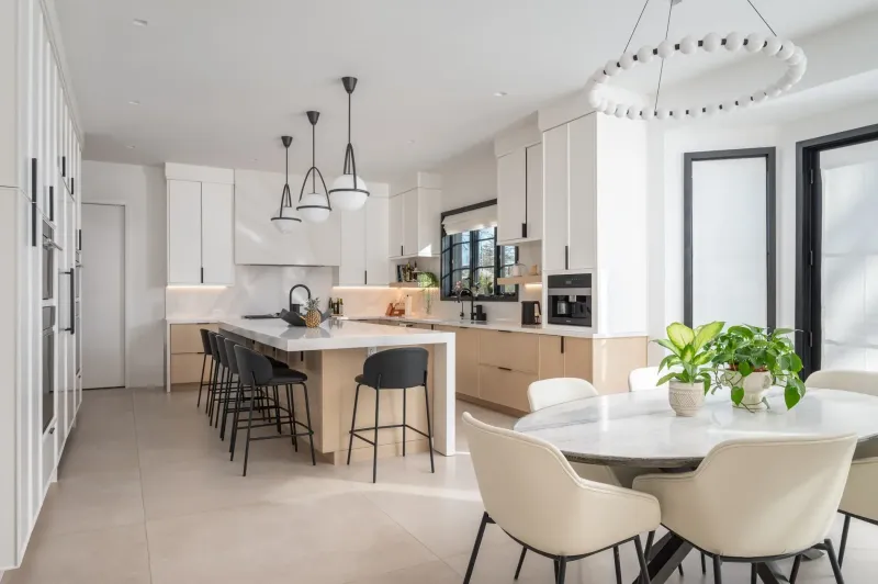 Kings Point Contemporary: an open white kitchen with a long island and black stools, three globe pendants, and the round dining table under a ring chandelier