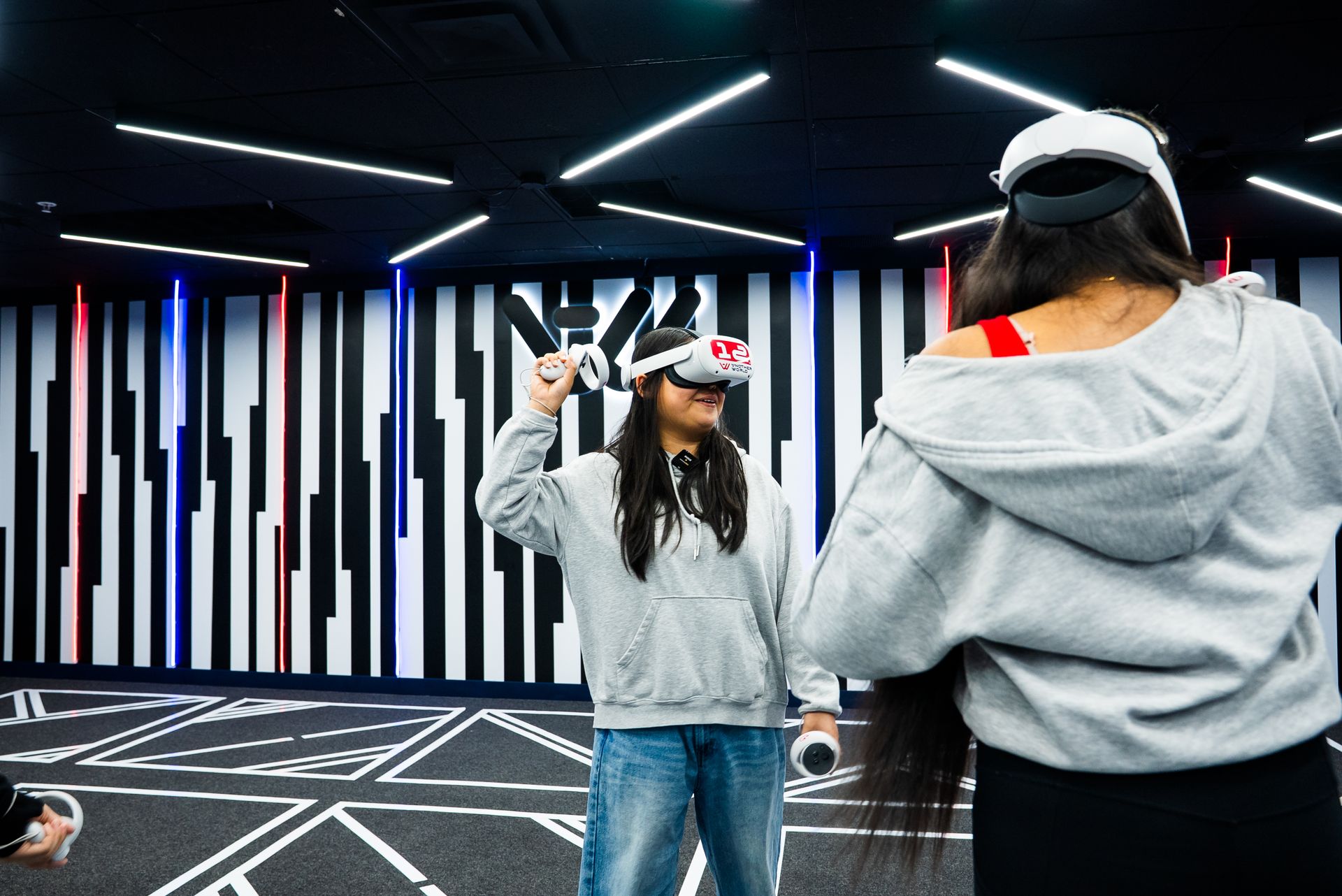 Two students in front of the striped logo wall, one reaching up