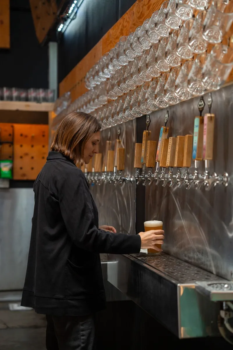 A bartender pouring a beer at the tap wall under rows of glasses