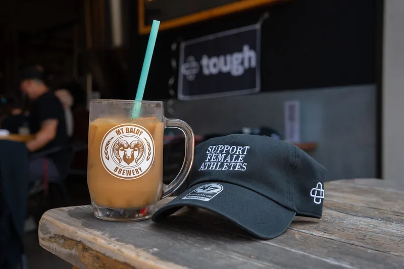 A Mt Baldy Brewery mug with a straw next to a Mt Baldy cap on the bar