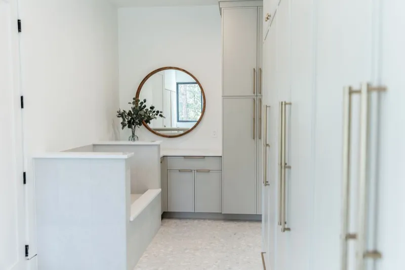 Utility room with sage green cabinets, a round mirror and a tiled built-in wash basin