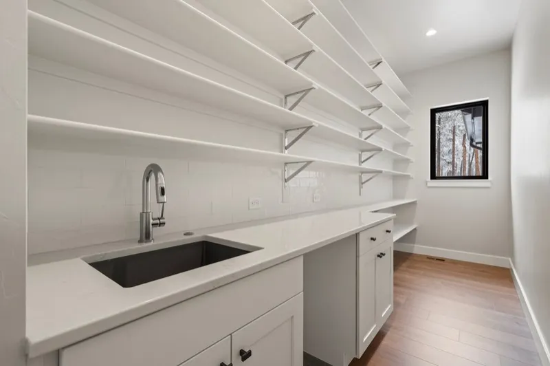 Walk-in pantry with white shaker cabinets, open shelving and an undermount sink