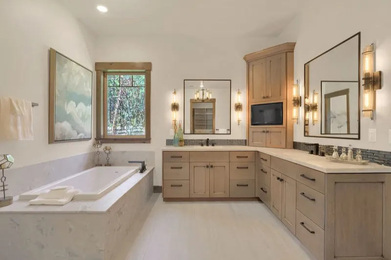 Primary bathroom with a light wood double vanity, soaking tub and wall sconces