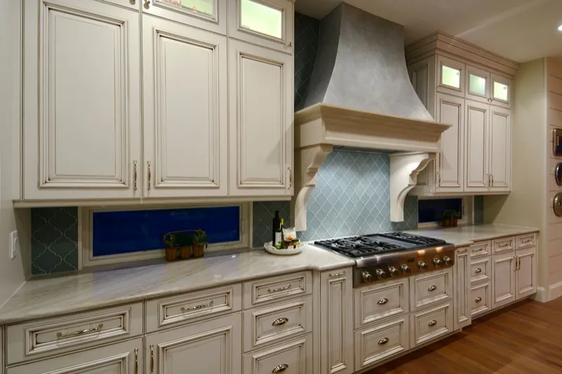Cream glazed raised-panel kitchen cabinets with a plaster range hood and arabesque tile backsplash
