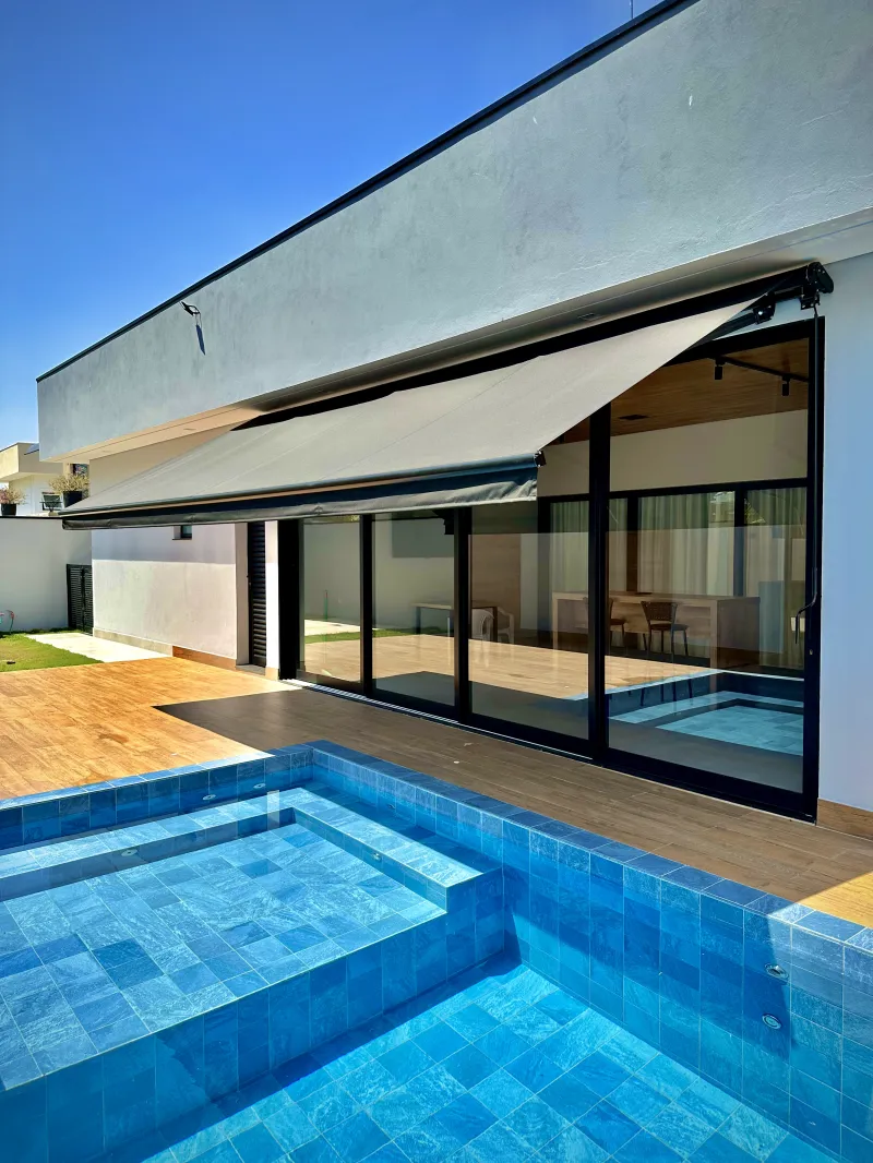 Toldo articulado em lona cinza protegendo deck de área gourmet do sol