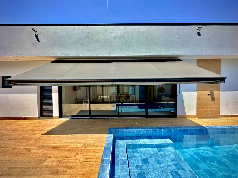 Toldo articulado motorizado aberto sobre área de piscina ao lado da casa
