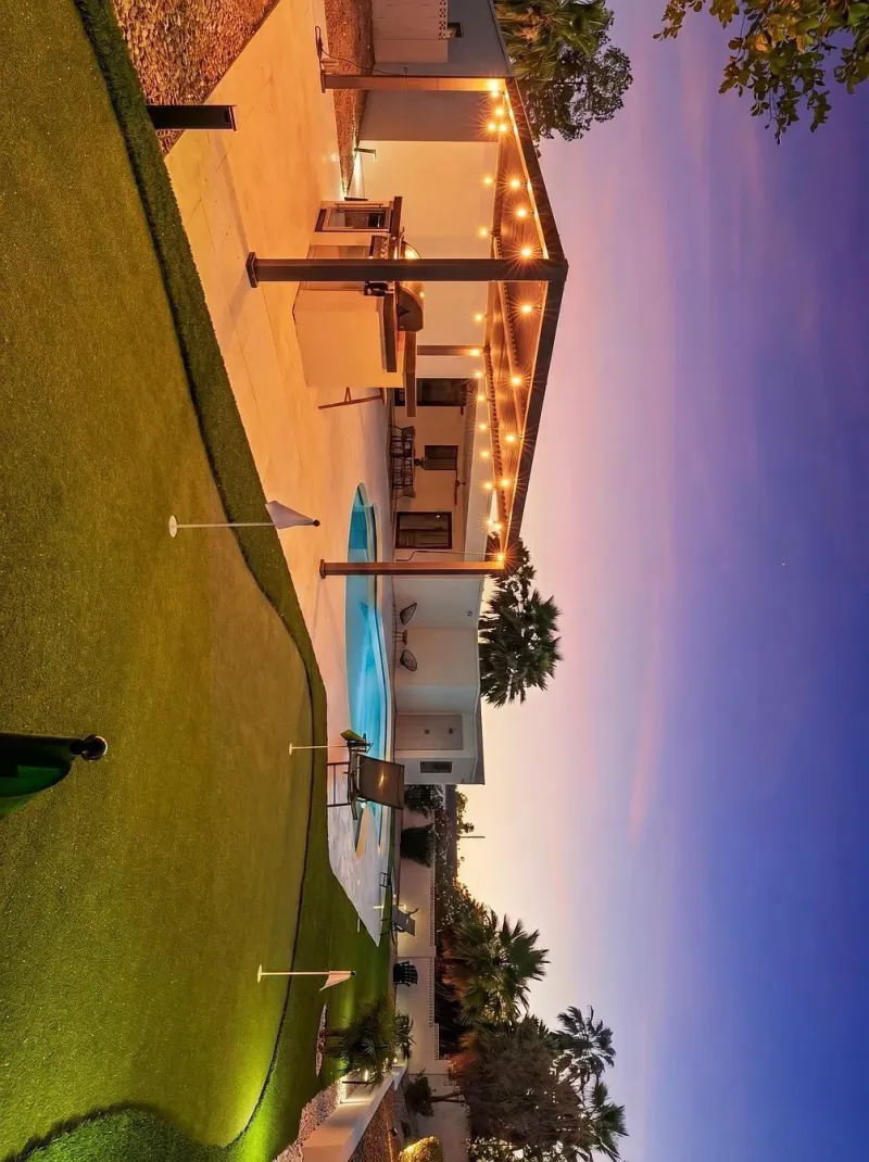 Backyard putting green at dusk with pergola string lights and pool — turf Phoenix AZ