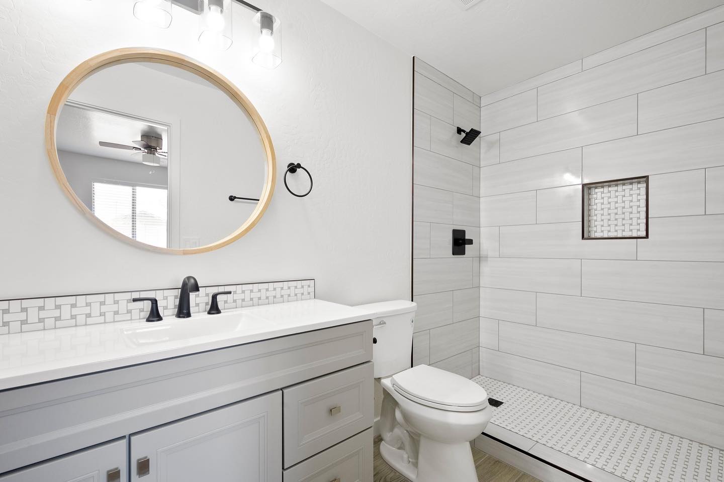 Modern bathroom with round wood mirror, black fixtures, and tile shower — bathroom remodel Phoenix AZ