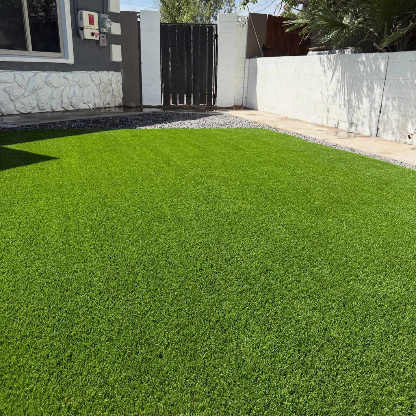 Side yard entrance with charcoal home, stone base, black gate, and lush turf lawn