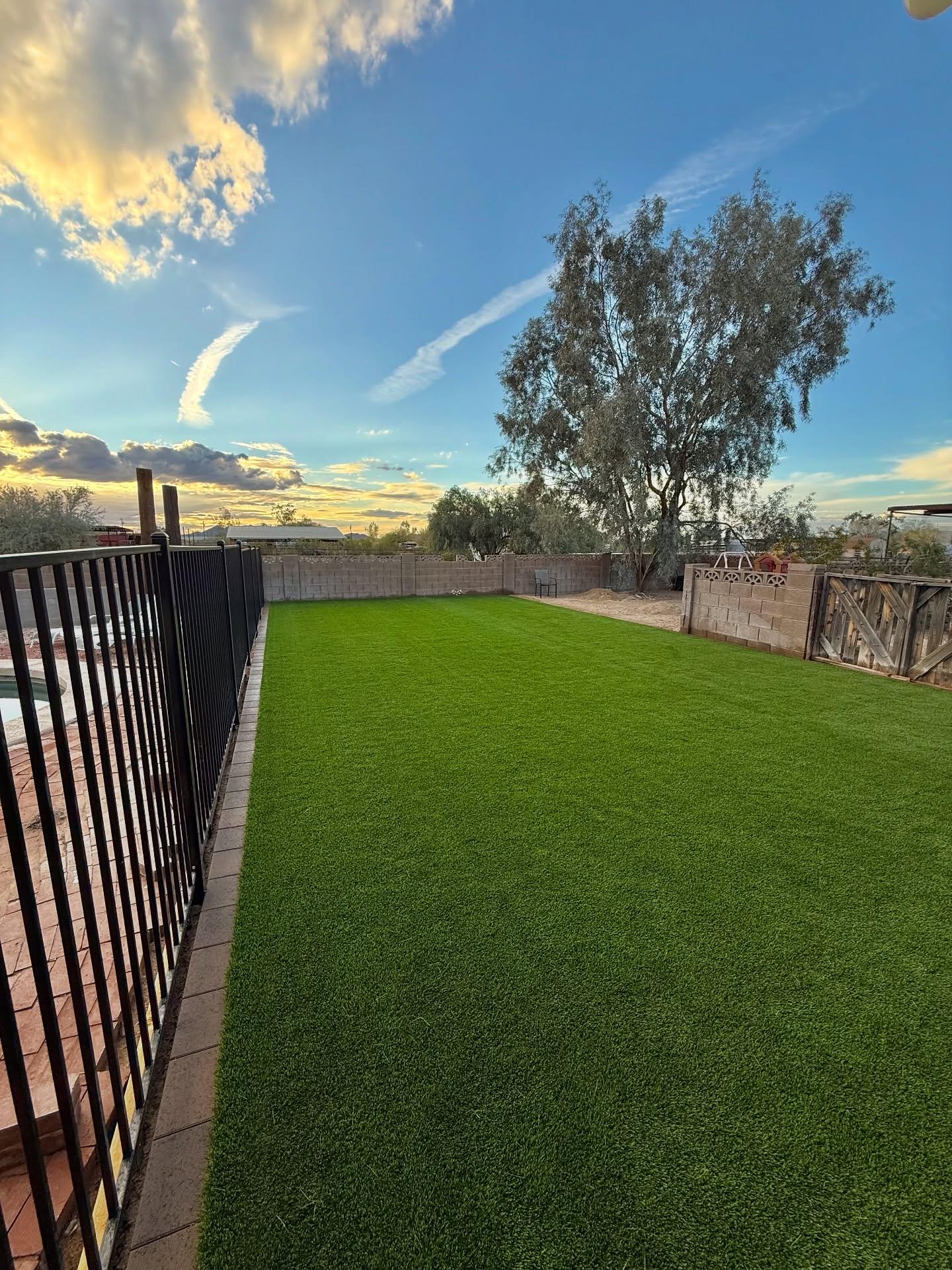 Backyard at dusk with paver-edged turf, pool fence, and golden Arizona sky, outdoor living Phoenix AZ