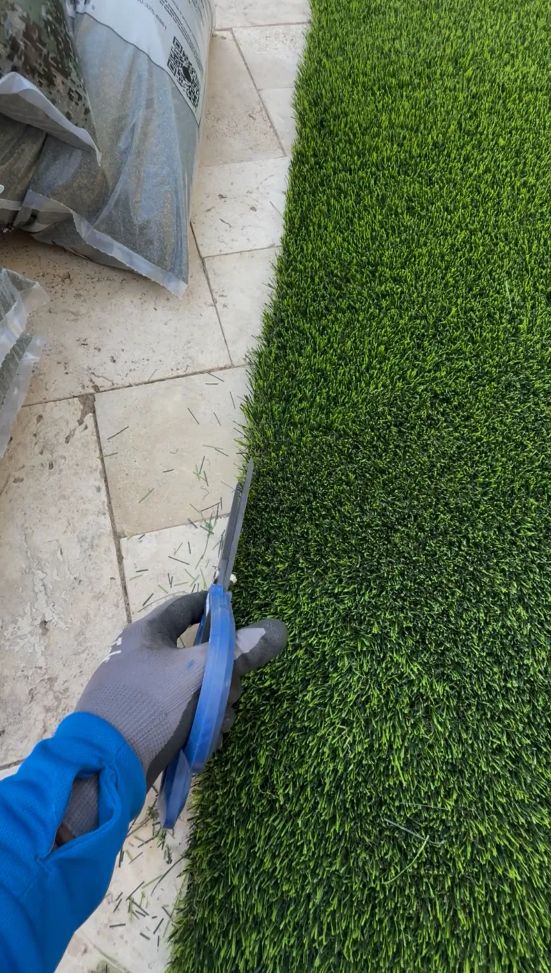 Installer custom-cutting artificial turf edge against travertine pavers, turf installation detail Phoenix AZ