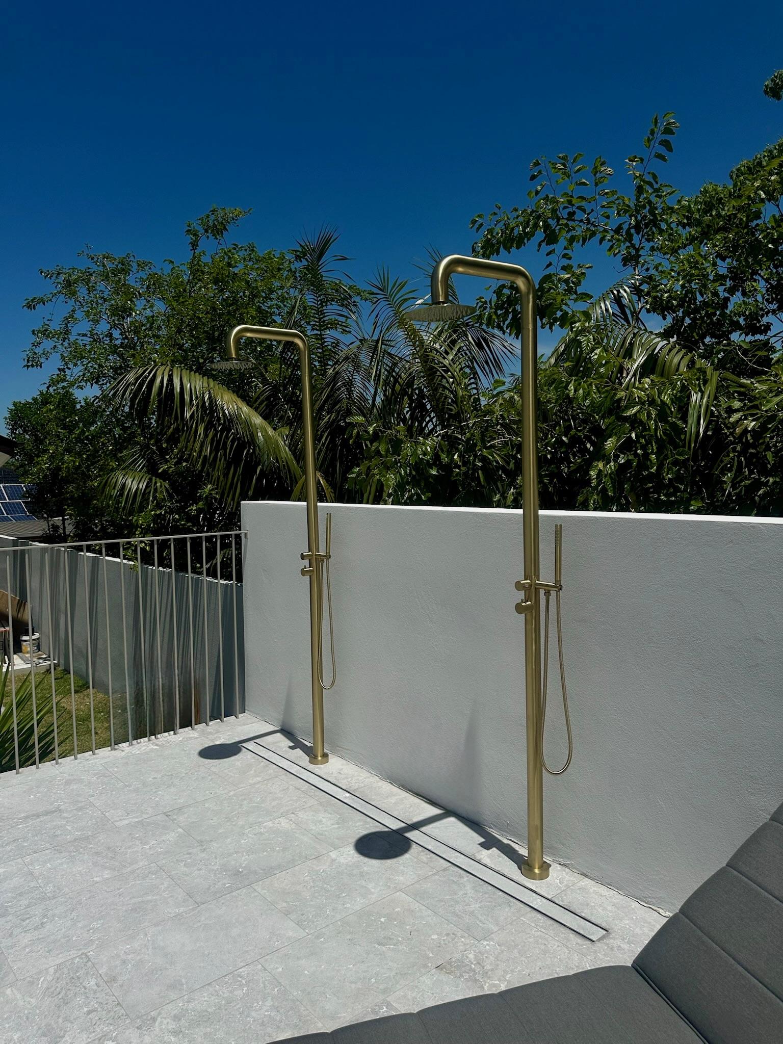 Two brass outdoor showers installed against a rendered wall