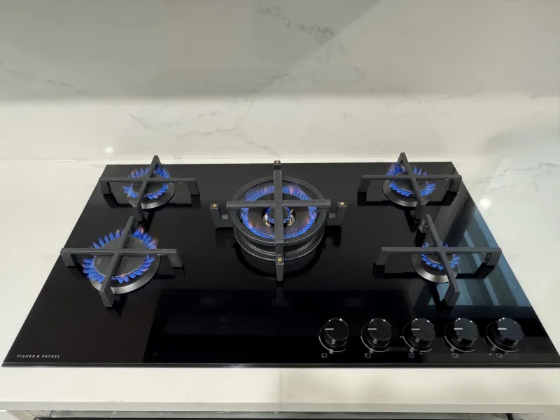 Five burner gas cooktop with every burner alight on a stone benchtop