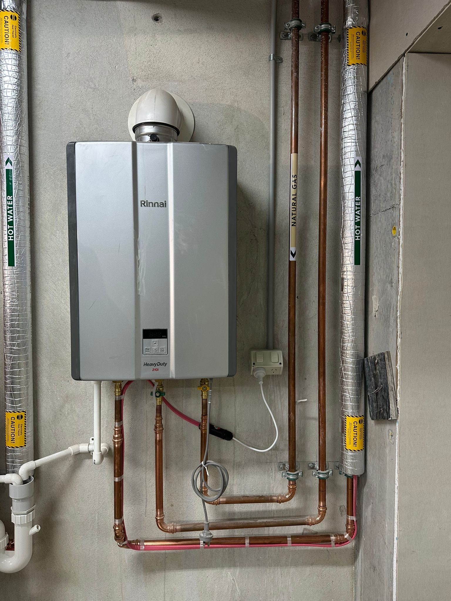 Internal gas water heater with a flue and labelled copper pipework