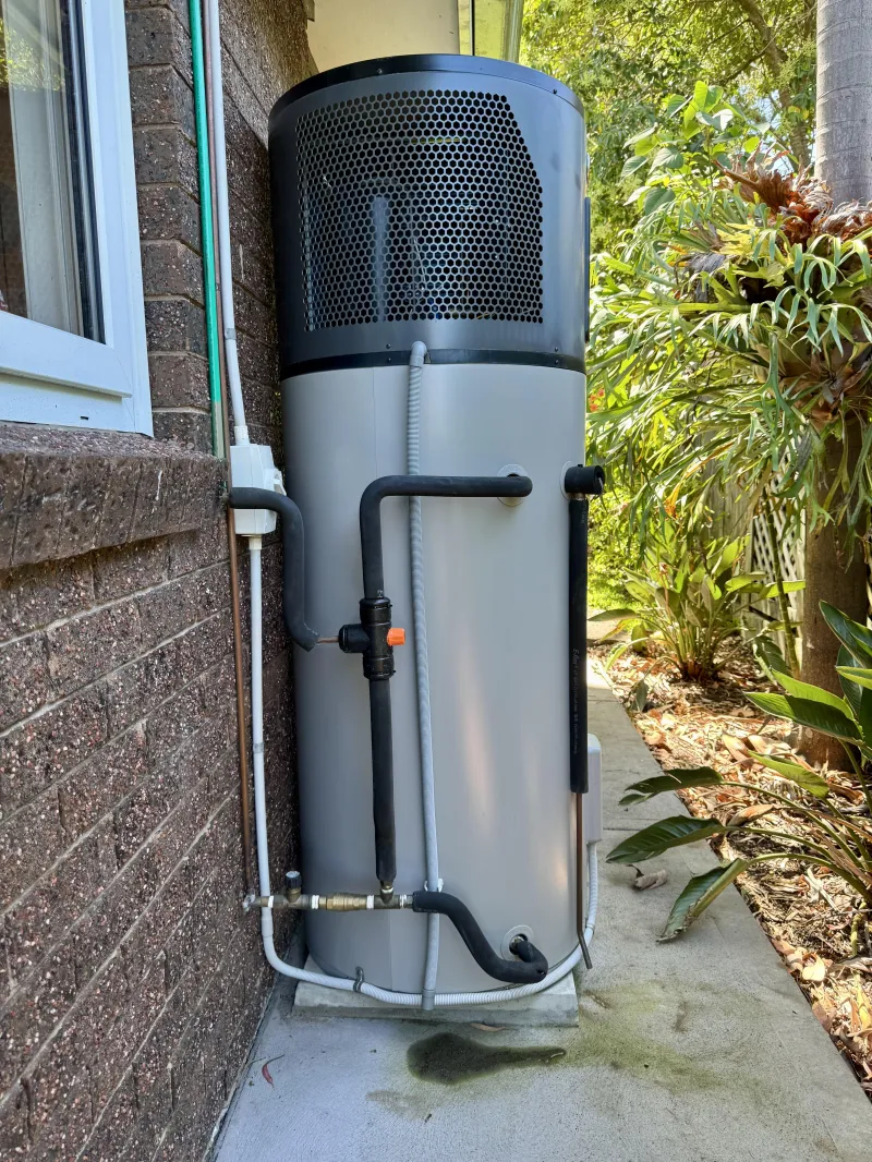Heat pump hot water unit installed beside a brick wall