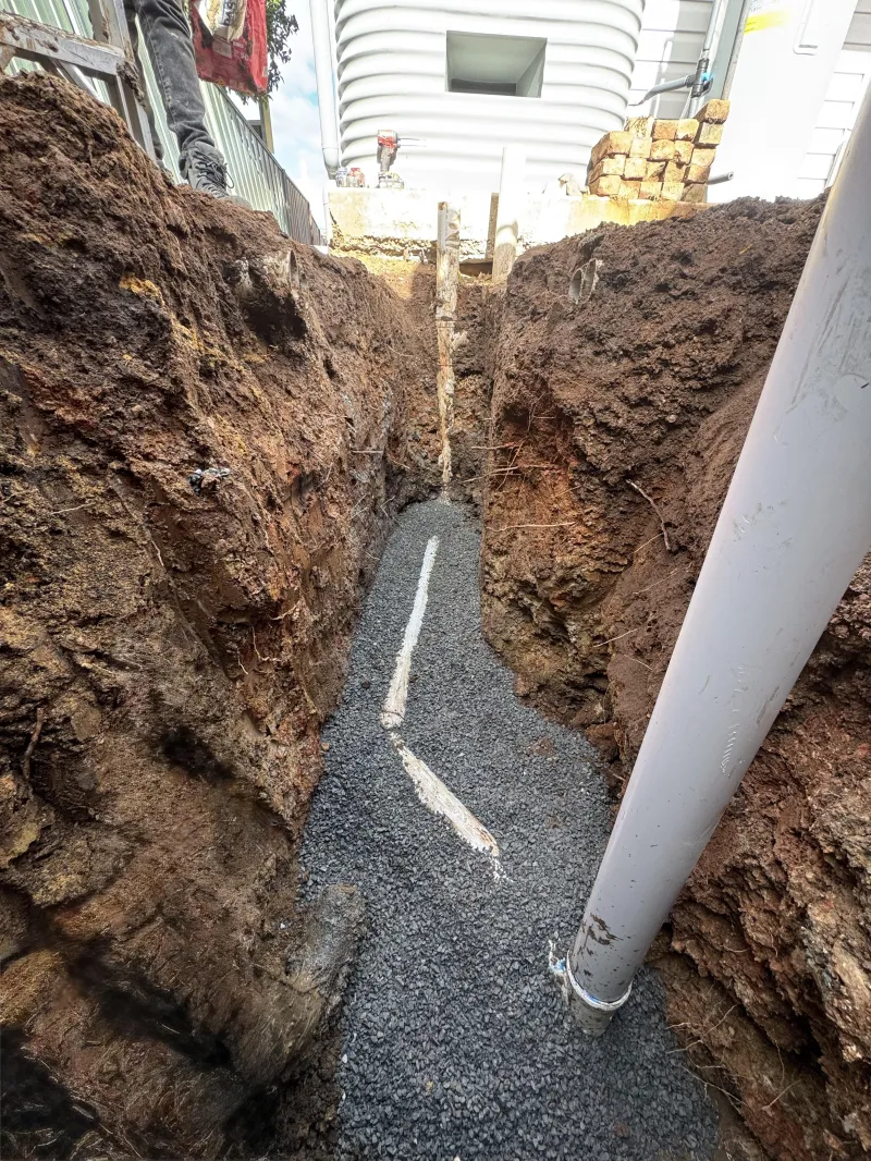Excavated trench with gravel bedding and new drainage pipe beside a building