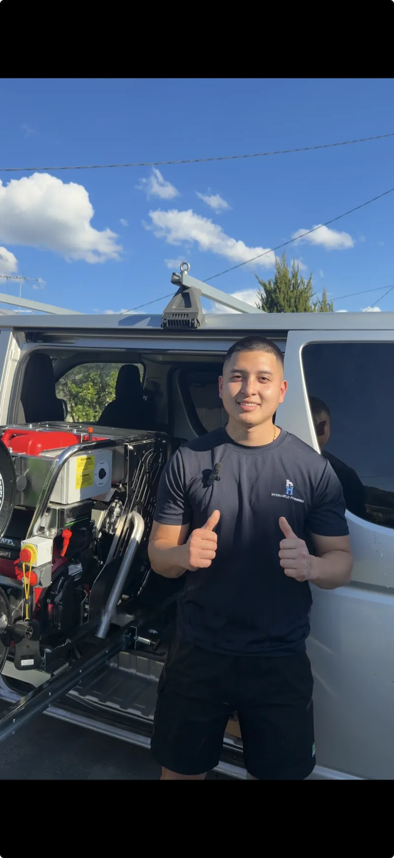 Plumber in a Hydrauflo Plumbing shirt standing beside a work van loaded with a jetting unit