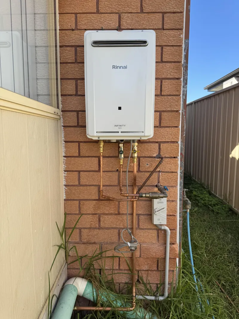 Continuous flow gas hot water unit on a brick wall with copper pipework and isolation valves