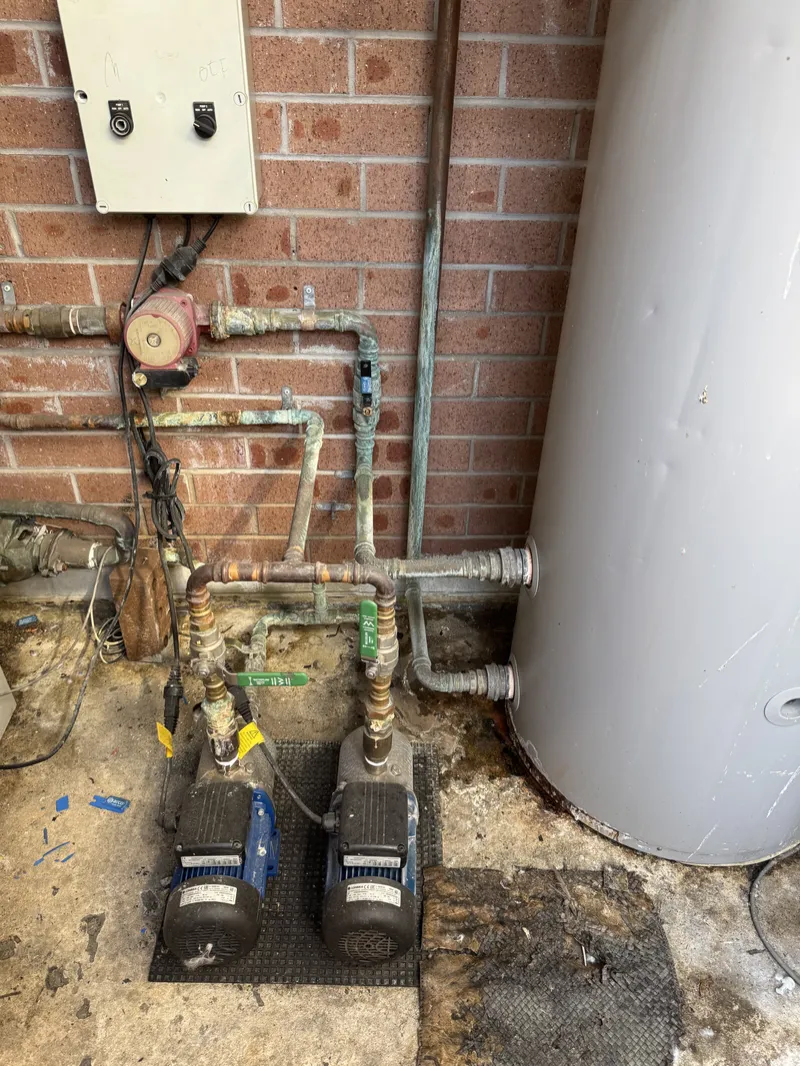 Hot water cylinder with pumps and copper pipework against a brick wall