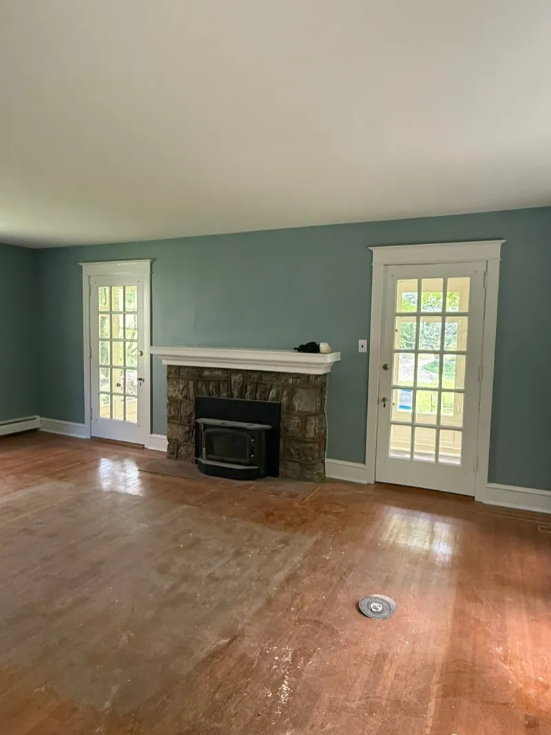 Living room painted sage green with stone fireplace and refinished hardwood