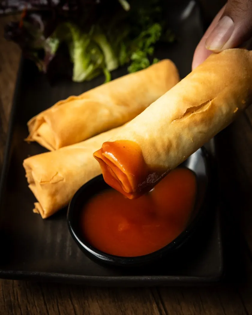 Crispy vegetarian spring rolls dipped in red sauce