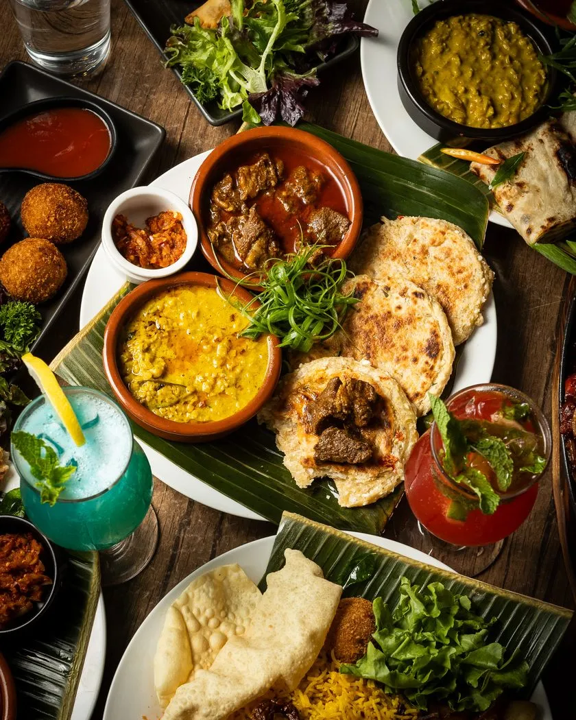 Overhead table spread of curries, roti, rice and drinks
