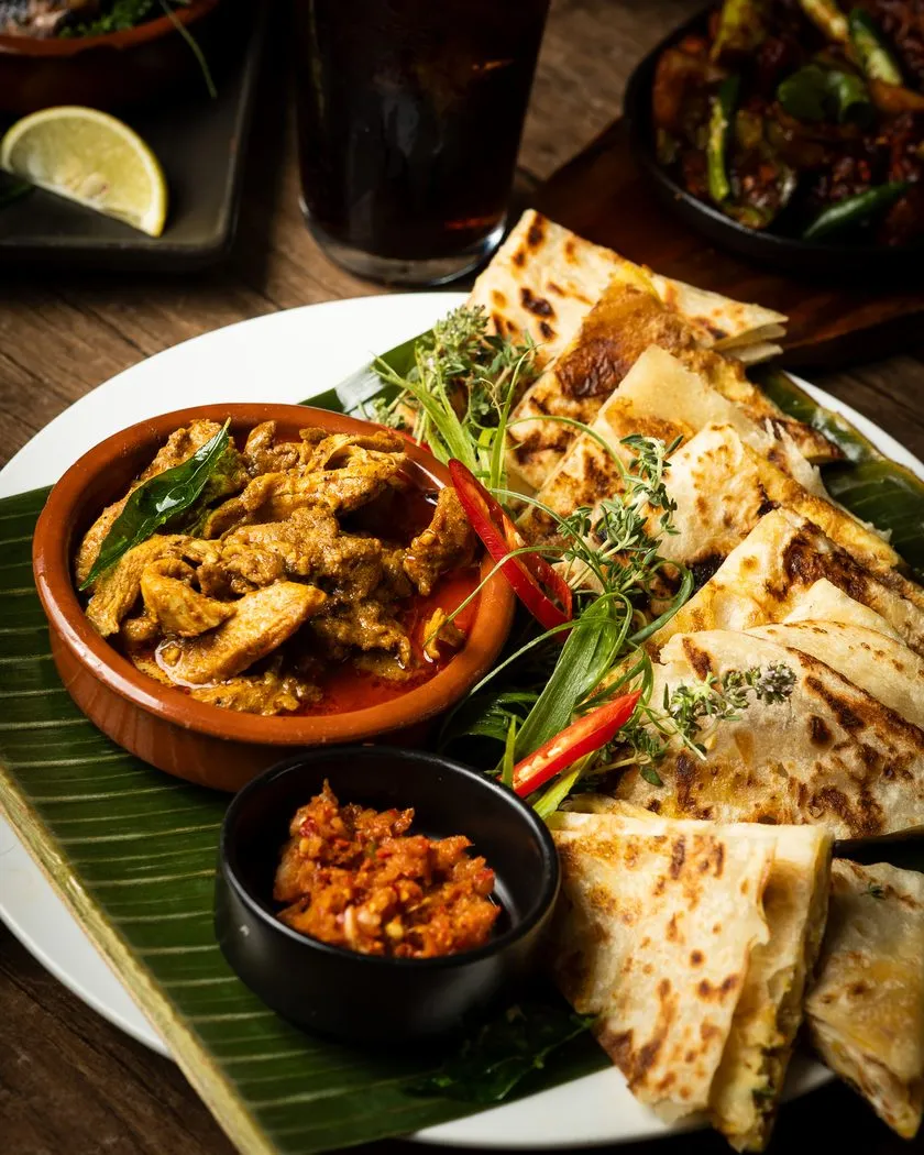 Curry in a clay pot served with roti and sambol on banana leaf