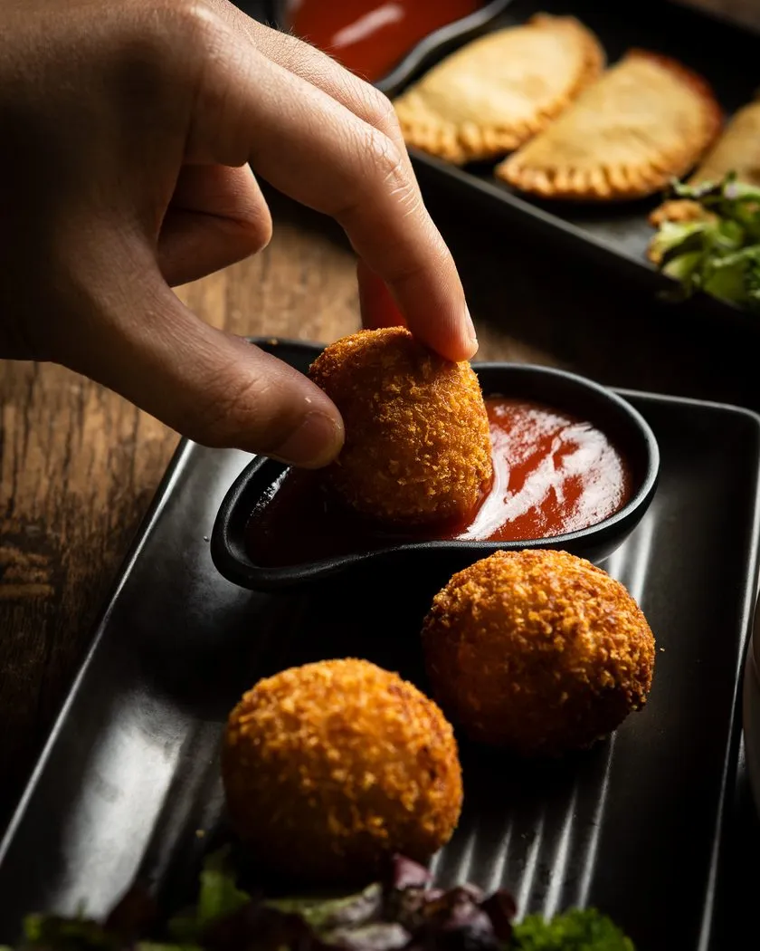 Golden Sri Lankan fish cutlet being dipped into chilli sauce